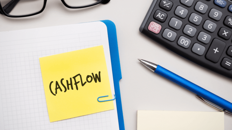 Cash flow note beside a calculator, notebook and pen